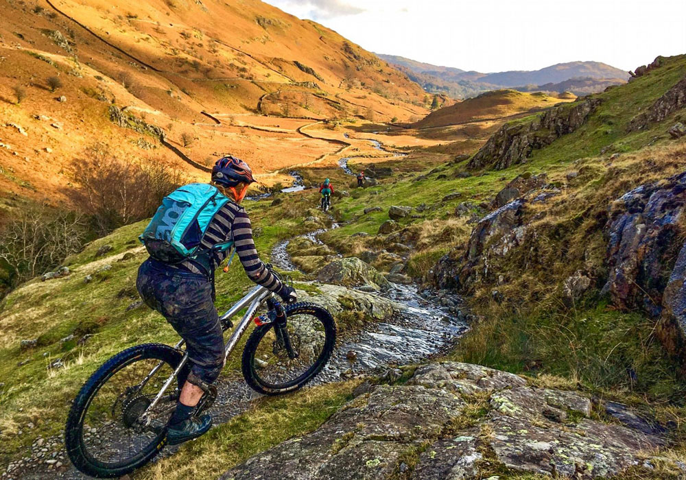 Woman mountain biking down a rocky trail in the Lakes