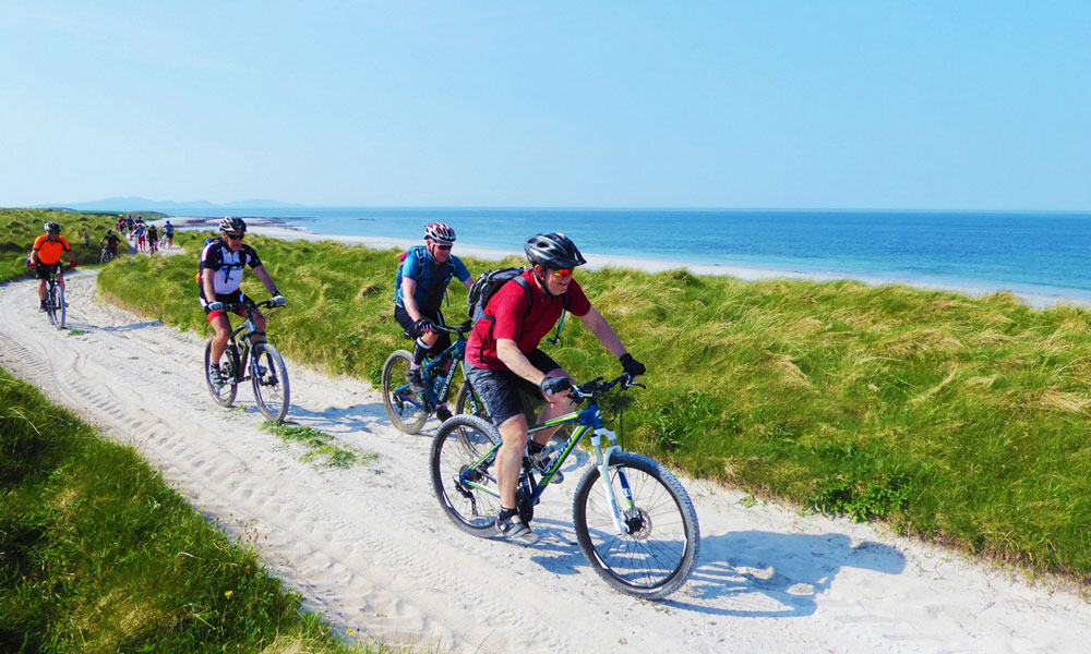 Hebridean Explorer - mountain bikers ride on white sand next to a beach in the Outer Hebrides