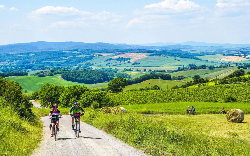 cyclists pedal along a track with rolling green hills behind