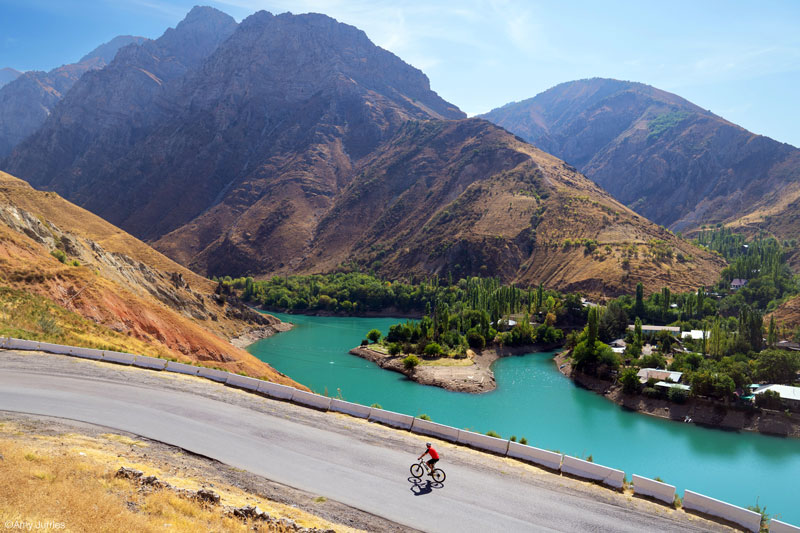 A cyclist against a backdrop of turquoise lack and mountains