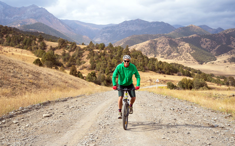 Cyclist rides an empty gravel trail with mountains behind